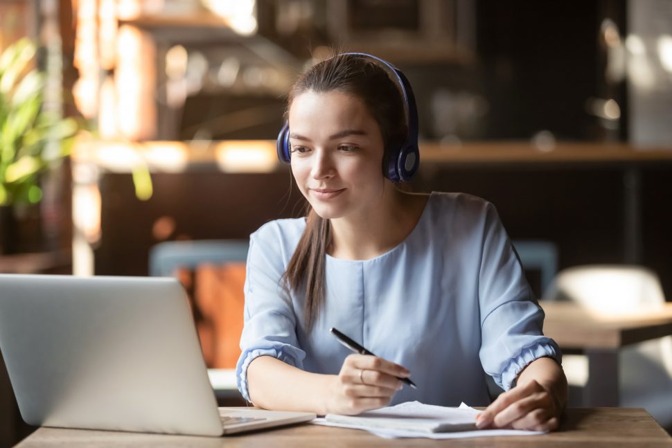 Focused woman wearing headphones using laptop, writing notes | FE Week