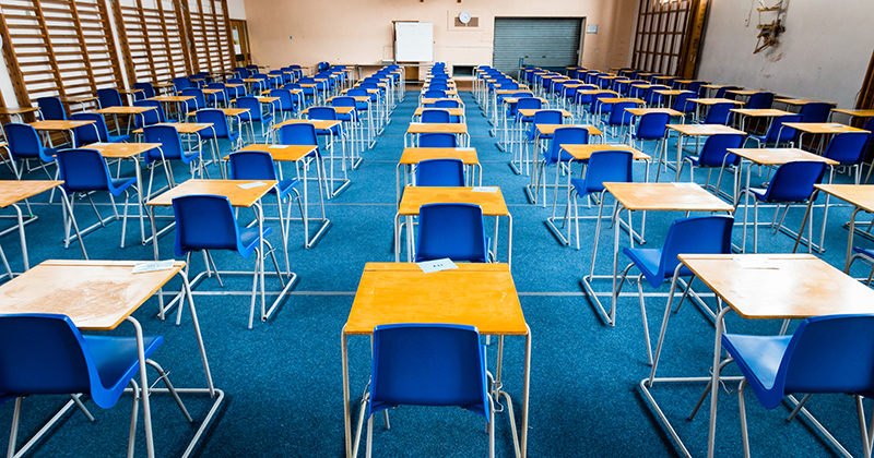 Empty exam desks set up in a school gym | FE Week